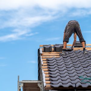 craftsman on the roof of a family house, building a roof covering from ceramic tiles.