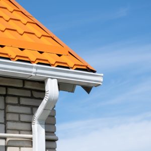 Rain Gutter Pipeline System on brick house , bright orange metal tile roof against blue sky