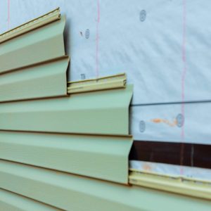 Construction worker carefully lays green siding on building exterior while ensuring proper fit.